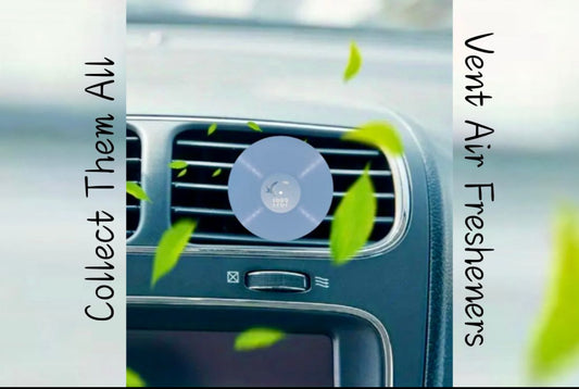 A car vent Air Freshener by featuring a blue circular vinyl record design, is clipped to a car vent as green leaves blow inside. Side text says, “Collect Them All” and “Vent Air Fresheners.”.