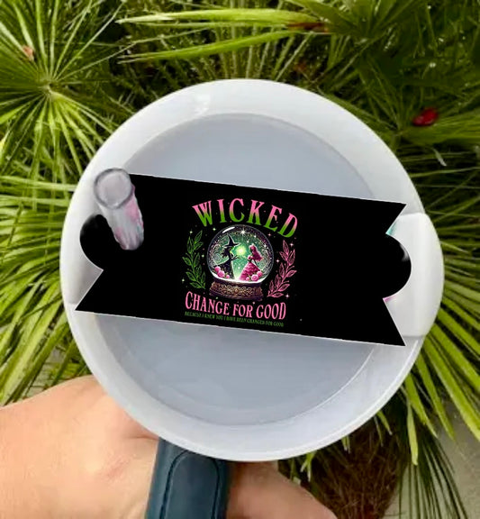 Amidst lush palm leaves, someone holds a watering can adorned with a vibrant green "Wicked Change for Good" sticker featuring two figures in a circle. This scene mirrors the fresh appeal of Kreative Kreationz's Wicked | Good Stanley Lid Topper.